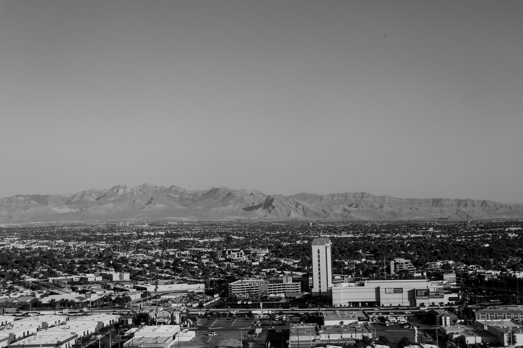 Black-and-white aerial view across a desert-basin city grid toward distant mountains