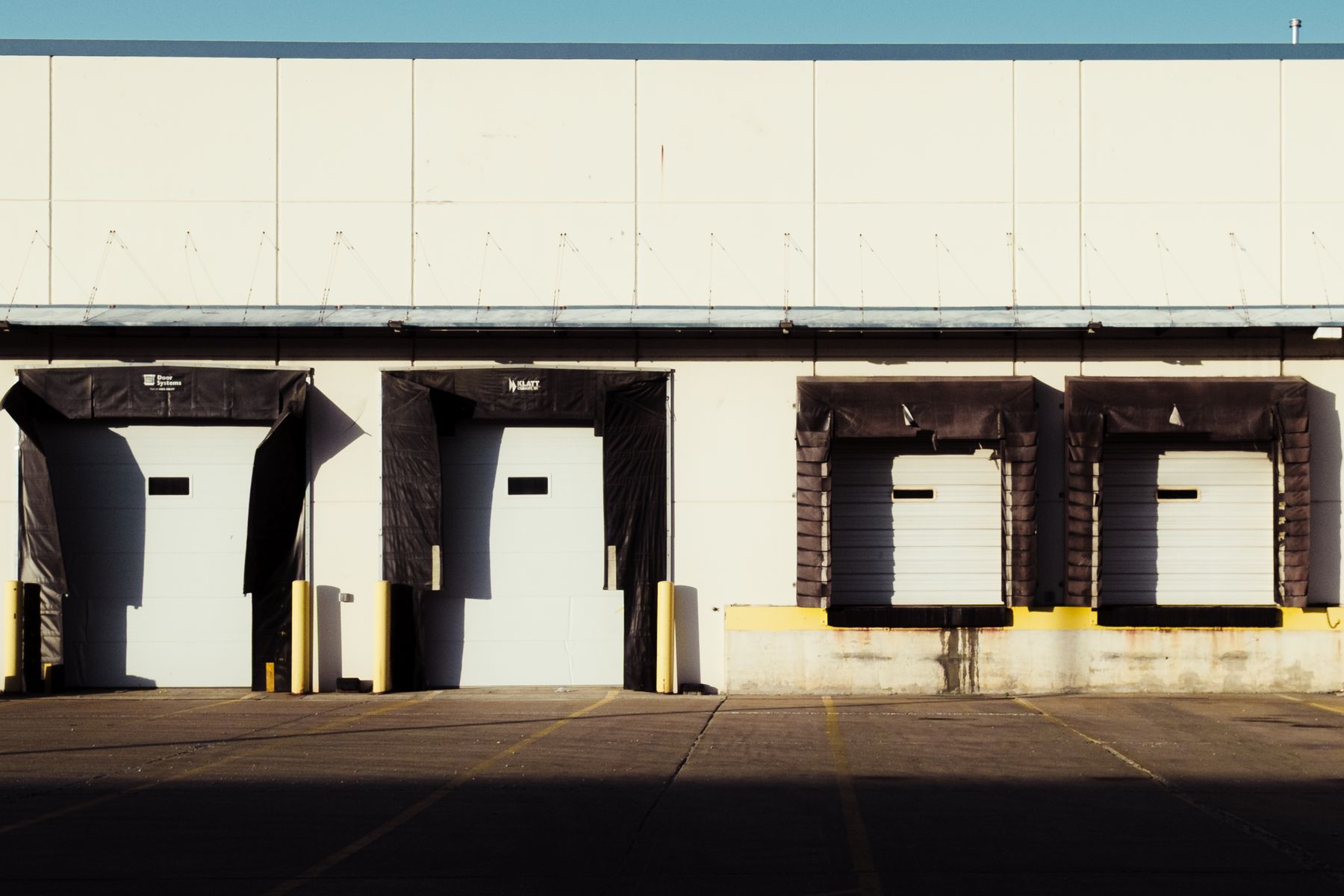 Sunlit row of closed warehouse loading bays along a concrete industrial facade